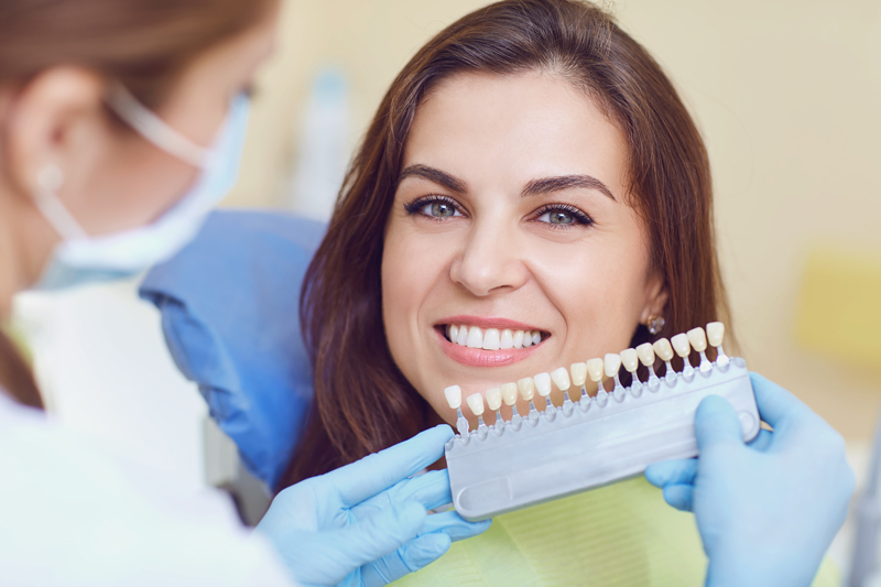 Image of a dentist holding a implant color matcher to a girls teeth
